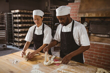 Multiracial mid adult male and female bakers braiding bread at table in bakery