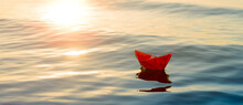 Paper Boat Sails Into The Sea, A Small Origami Ship On The Water In The Setting Sun, Travel Concept. Taking Trip