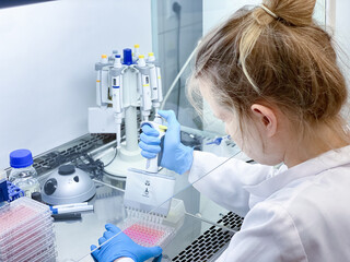 Wall Mural - A female PhD student performing a biological experiment on a cancer cells in a sterile environment of designated biosafety laboratory at research facility. 