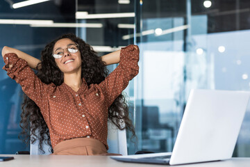 Young woman engineer developer programmer works in the office inside the IT company, satisfied with the work result, rests hispanic looks out the window, smiles hands behind her head, dreams.