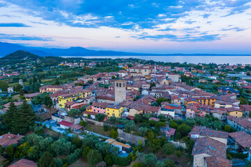 Aerial view of village near Lago di Garda Italy. Beautiful sunset light. Flying close to the church tower revealing Lago di Garda on the horizon. Manerba del Garda town in Brescia Italy.  