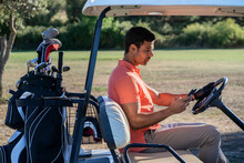 Golfer Chatting On Smartphone In Golf Cart In Countryside Field