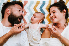 Happy Parents Having Fun While Relaxing With Infant Together On Bed