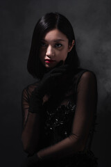 Wall Mural - portrait of young asian woman in gothic outfit and gloves looking at camera on grey with smoke.