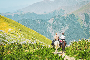 Two caucasian girls on white and brown horse ride in caucasus mountains together on black rock lake hike trail in Georgia