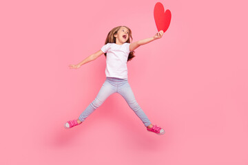 Wall Mural - Full body portrait of overjoyed carefree girl jump arm hold large paper red heart isolated on pink color background