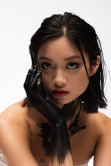 Wall Mural - brunette young asian woman with hand in black paint looking at camera isolated on white.