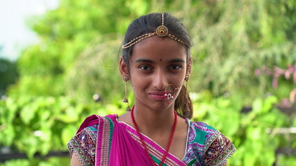 Portrait of smiling Indian girl wearing traditional colorful rajasthani outfit and jewelery against green background. Portrait of a India Rajasthani girl. Navratri festival concept.