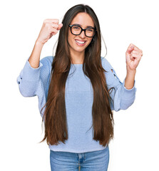 Sticker - Young hispanic girl wearing casual clothes and glasses screaming proud, celebrating victory and success very excited with raised arms