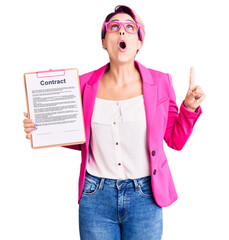 Sticker - Young beautiful woman with pink hair holding clipboard with contract document amazed and surprised looking up and pointing with fingers and raised arms.