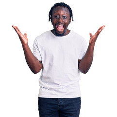 Canvas Print - Young african american man with braids wearing casual white tshirt celebrating crazy and amazed for success with arms raised and open eyes screaming excited. winner concept