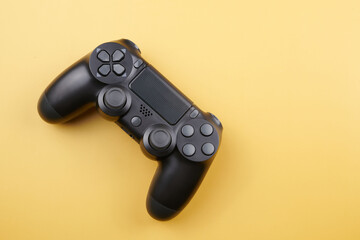 Black video game controller, joystick for game console isolated on yellow background. Gamer control device close-up