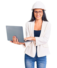 Poster - Young beautiful latin girl wearing architect hardhat holding laptop looking positive and happy standing and smiling with a confident smile showing teeth