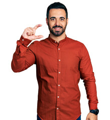 Poster - Young hispanic man with beard wearing casual shirt smiling and confident gesturing with hand doing small size sign with fingers looking and the camera. measure concept.