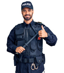 Wall Mural - Young hispanic man wearing police uniform holding baton smiling happy and positive, thumb up doing excellent and approval sign