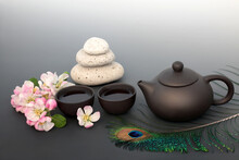 Japanese Tea Ceremony For Inner Peace With Pebble Stack, Ceramic Tea Set, Apple Blossom Flowers, Peacock Feather. Zen Balance And Mindfulness Concept On Gradient Grey.