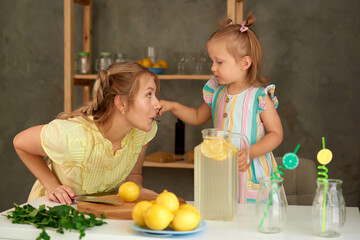 Wall Mural - little daughter gives mom to try lemonade from spoon in kitchen