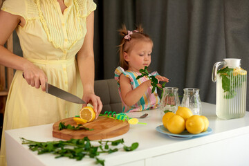 Wall Mural - woman with little daughter make homemade lemonade with fresh yellow lemons and green mint. shallow depth of field closeup photo