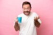 Middle age caucasian man holding cup of coffee isolated on pink background with shocked facial expression