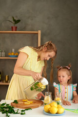 mom pours cool refreshing lemonade from a jug into a glass for her little daughter in the kitchen