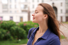 Portrait Of Beautiful Attractive Happy Girl Young European Woman Is Enjoying Good Summer Sunny Day In The City, Yard Or Park With Eyes Closed, Breathing Deeply Deep Fresh Air Smiling