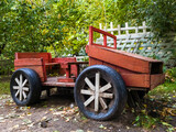 Fototapeta Sypialnia - Wooden red handmade vintage car for children fun playing stand in a park at autumn day.