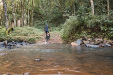 Unrecognizable Cyclist Riding Bicycle In Shallow River In Forest
