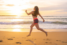 Fit Sportswoman Running Along Sandy Beach At Sunset