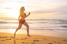 Fit Sportswoman Running Along Sandy Beach At Sunset