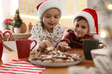 cute little children taking tasty christmas cookies from plate at table in kitchen