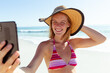 © wavebreak3 - Caucasian woman at beach wearing a hat and taking selfie with her smartphone