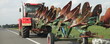 © Ilya - Big tractor drive with ploughing machine on trailer on countryside asphalt road at summer day - harvesting, agriculture, farming in East Europe