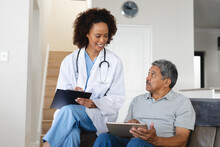 Senior Mixed Race Man With Female Doctor Home Visiting Talking Using Tablet