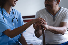 Senior Mixed Race Man With Female Doctor Home Visiting Holding Hands