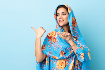 Sticker - Young Moroccan woman with traditional costume isolated on blue background pointing to the side to present a product