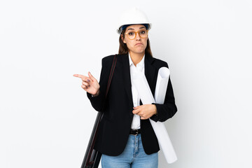 Sticker - Young architect caucasian woman with helmet and holding blueprints over isolated background pointing to the laterals having doubts