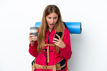 Wall Mural - Young mountaineer girl with a big backpack over isolated white background holding coffee to take away and a mobile