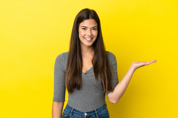 Wall Mural - Young Brazilian woman isolated on yellow background holding copyspace imaginary on the palm to insert an ad