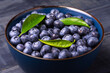 Blueberries with green leaves in a bowl, on a dark blue wooden background. Close-Up. Healthy food. Diet. Top view.