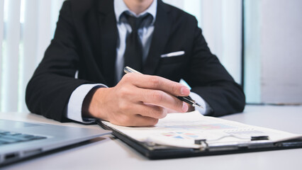 Close-up a business hand signing documents for approval, agreement with partners, working on laptop computer on desk in modern office