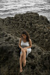 © Nina - A sadness woman is sitting on the rock. A curly-haired female in depression. Pensive brunette girl in white dress crying and worry at the sea. Dark photography