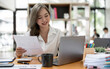 © NAMPIX - Smiling woman sitting at her desk in office. Happy business woman sitting in office working on laptop and paperwork.