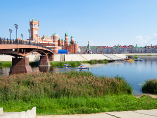 Wall Mural - overgrown waterfront near Voskresenskiy bridge and view of Patriarch's square on embankment of Malaya Kokshaga river in center of Yoshkar-Ola city on sunny summer day