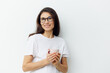 © Tatiana - a sweet, beautiful, pleasant woman in glasses and a white t-shirt stands holding a cup in her hands and smiles sweetly.Horizontal photo on a light background