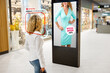 Woman walking in store while futuristic artificial intelligence advertising screen showing to consumer personalized promotion offers