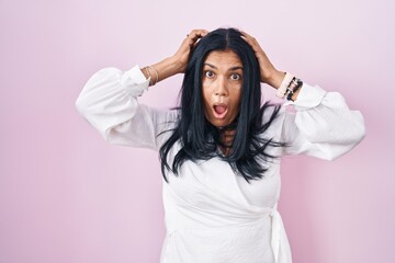 Poster - Mature hispanic woman standing over pink background crazy and scared with hands on head, afraid and surprised of shock with open mouth