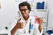 © Krakenimages.com - African doctor man holding pink cancer ribbon smiling happy and positive, thumb up doing excellent and approval sign