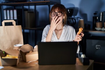 Young beautiful woman working using computer laptop and eating delivery food bored yawning tired covering mouth with hand. restless and sleepiness.