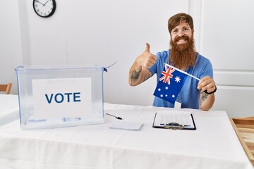 Canvas Print - Caucasian man with long beard at political campaign election holding australia flag smiling happy and positive, thumb up doing excellent and approval sign