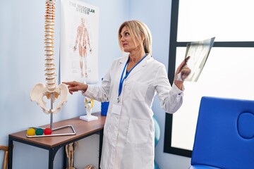 Canvas Print - Middle age blonde woman wearing physiotherapist uniform holding xray at physiotherapy clinic